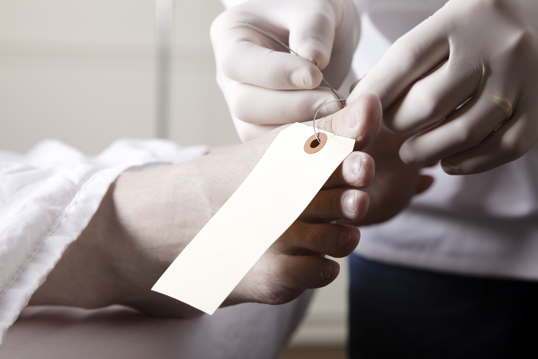 close up of gloved hands putting a tag on a body&#x27;s toe