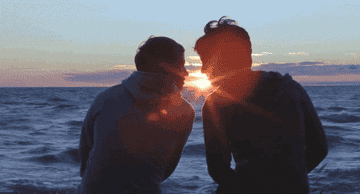 two guys kissing in front of a sunset on the beach