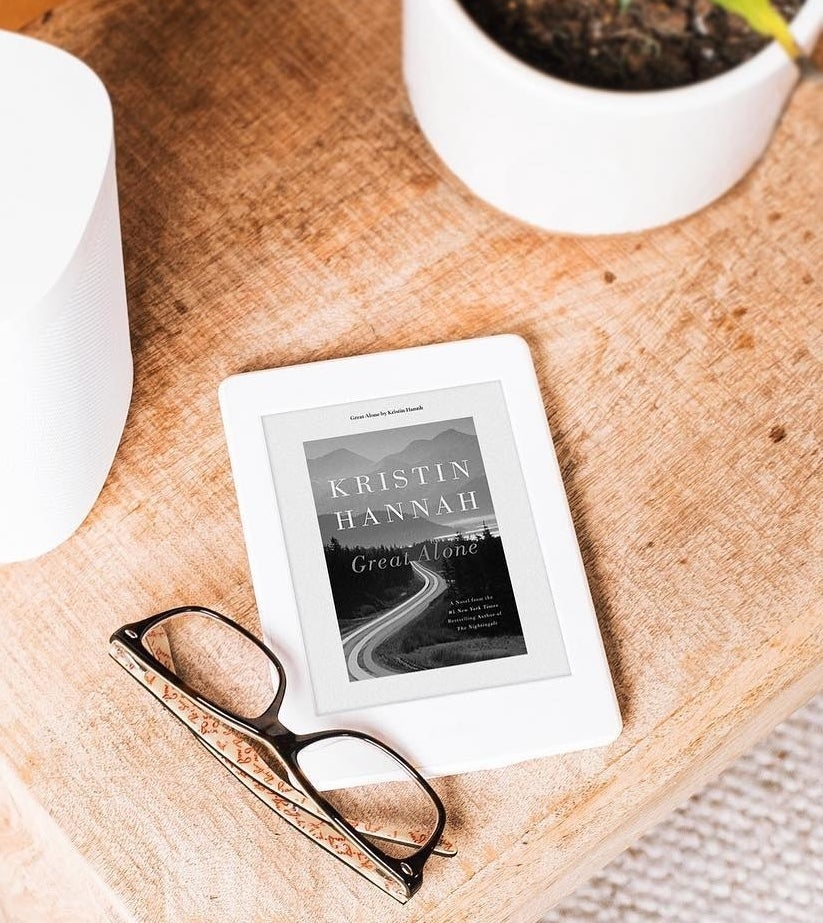 a kindle next to a pair of reading glasses on a desk