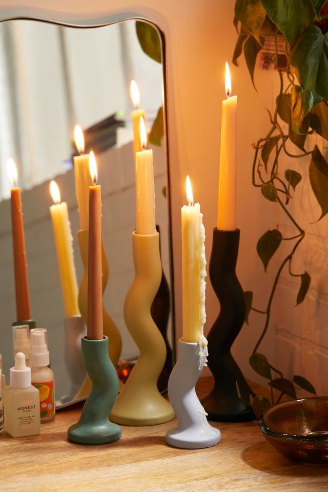 several taper candles in various holders on a vanity
