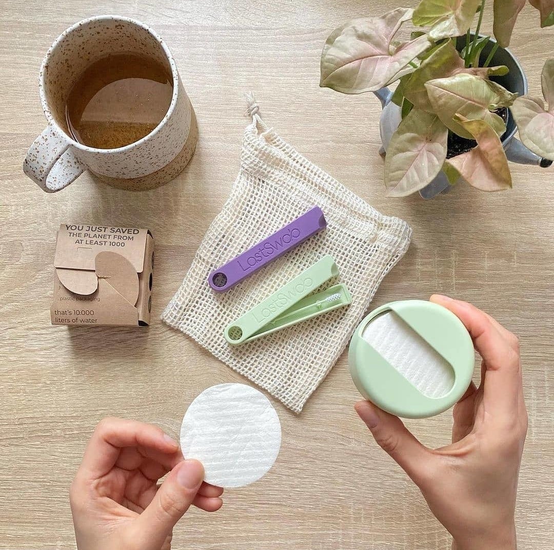 a person holding a case with reusable makeup pads above a cup of tea and two swabs