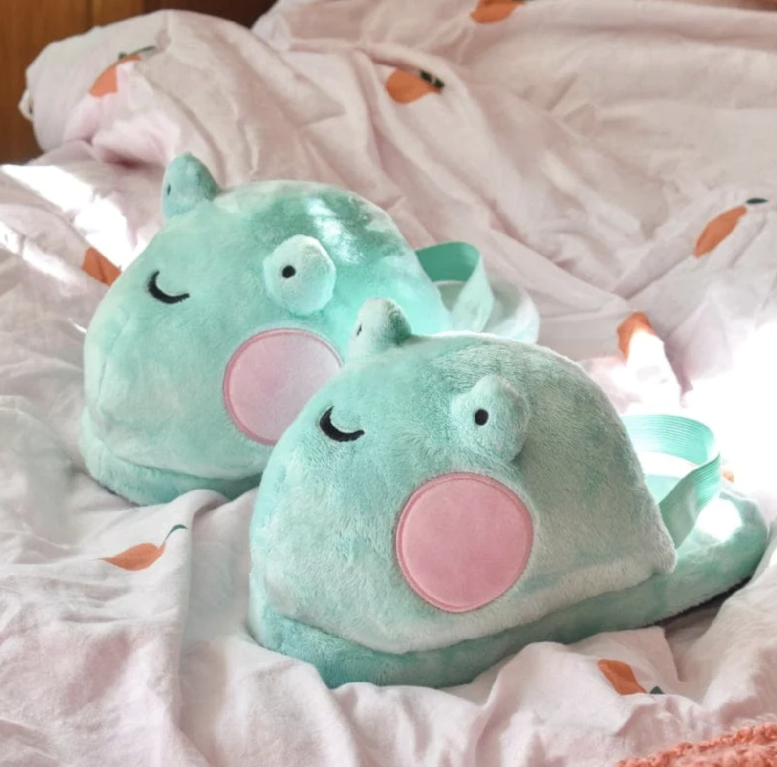 two frog slippers on a cozy bed