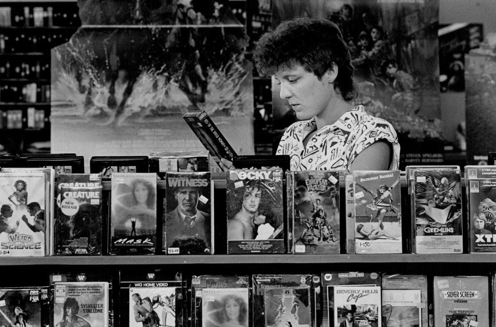 A person in a black-and-white photo looking through VHS tapes at a video rental store