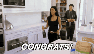 Kourtney Kardashian walks into a room holding bottles of champagne while saying &quot;congrats!&quot;