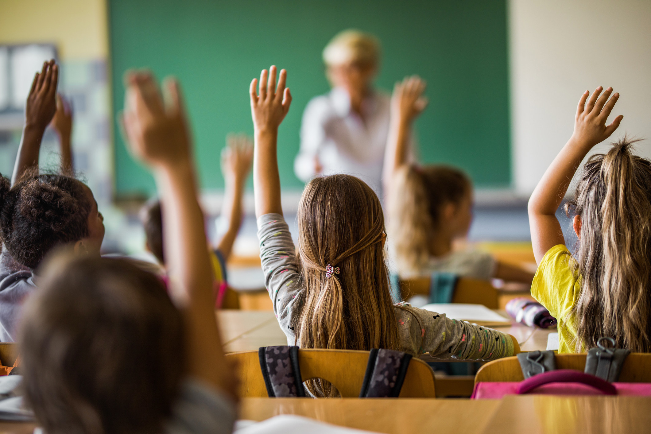 A class of children raise their hands in a classroom