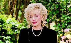 Dolly Parton is dressed in black and cries, wiping her nose with a tissue. 
