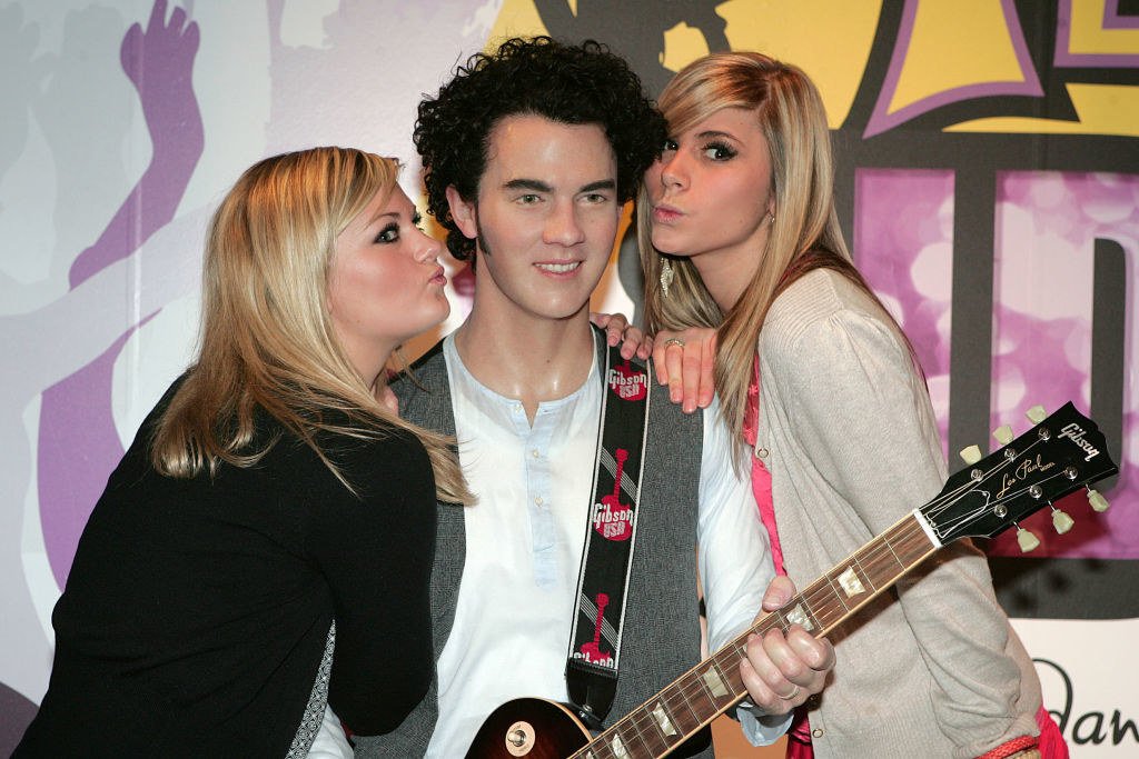 Two women pretending to kiss the wax figure, which is holding a guitar