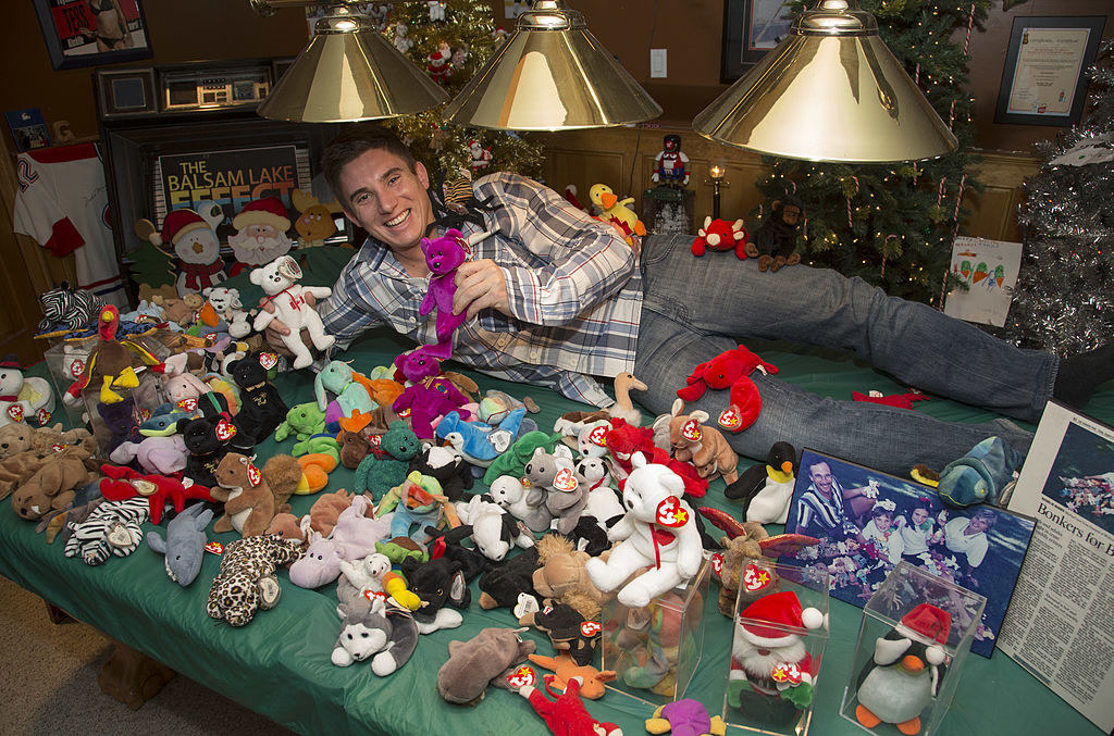 A man lying on a bed and surrounded by Beanie Babies and a newspaper article about him