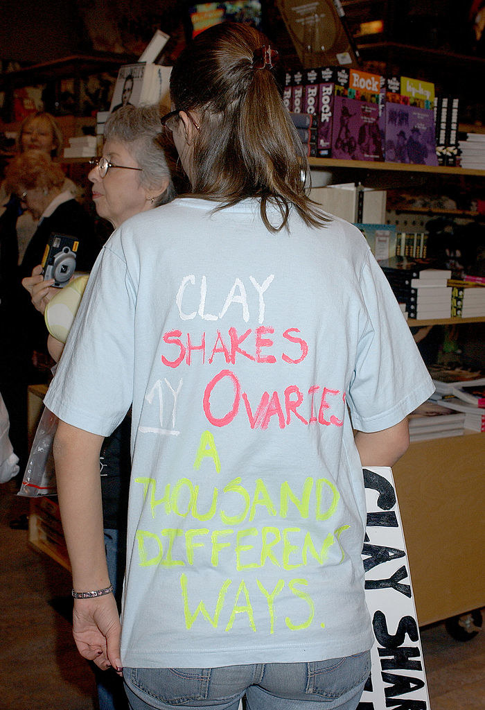 Back of a T-shirt worn by a woman, with the text &quot;Clay shakes my ovaries a thousand different ways&quot;