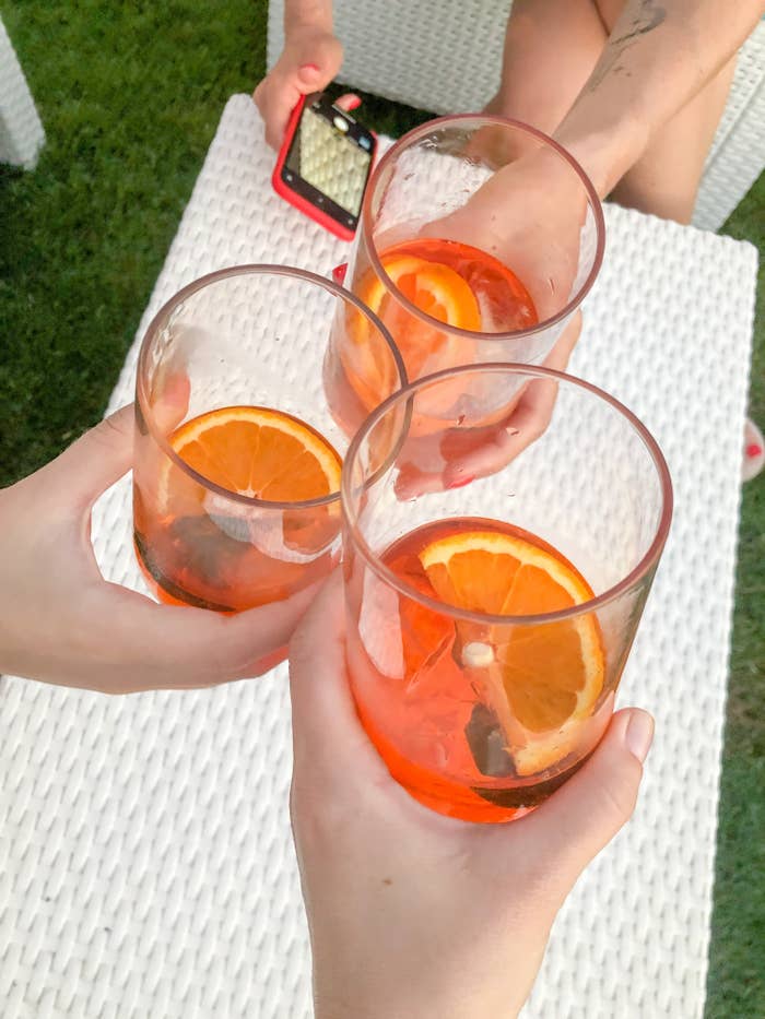 Three people cheers with Aperol spritz in cocktail glasses outside