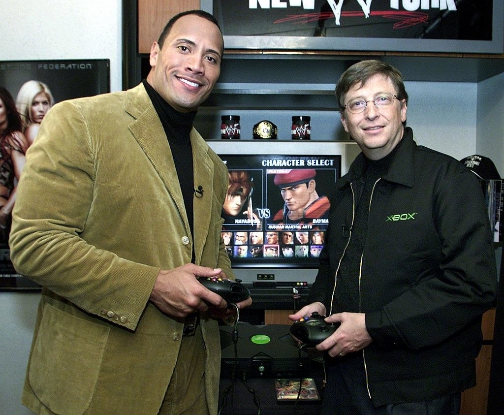Dwayne and Bill standing and holding game controllers in front of a video game