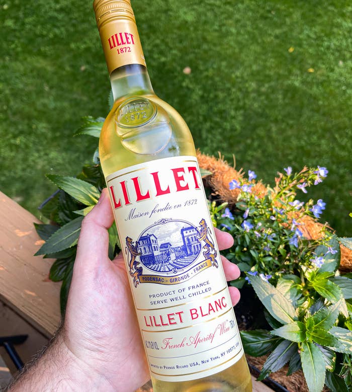 holding a bottle of Lillet in front of a flower window box