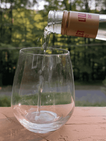 Pouring Lillet into a wine glass with trees in the background