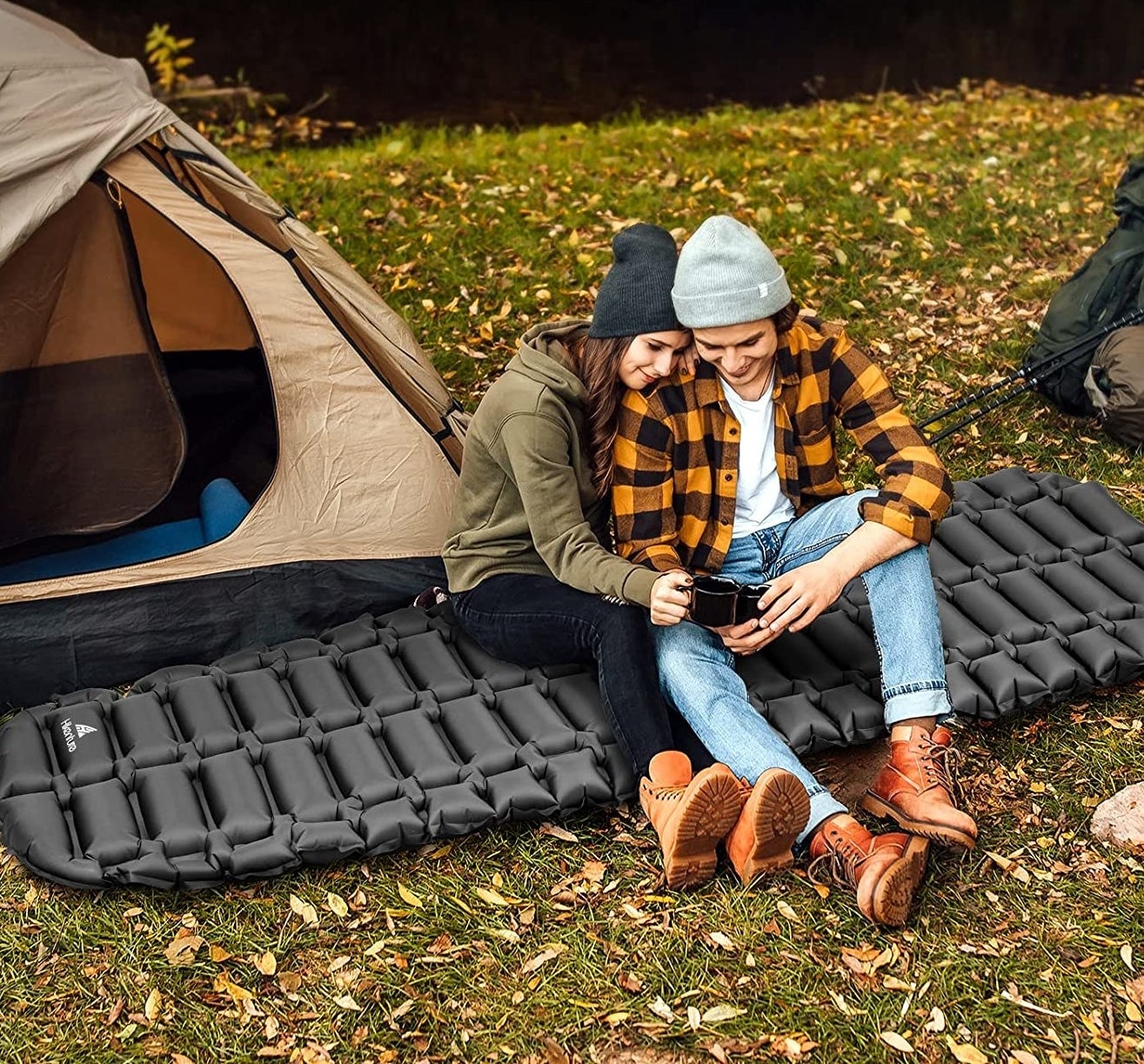 two people sitting on the sleeping pad outside in front of a tent