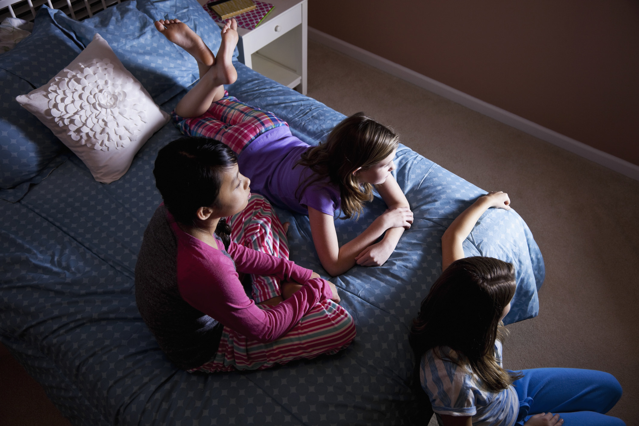 Three girls sit on a bed at a sleepover