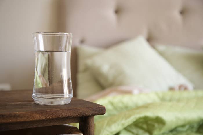 Glass with water on a wooden nightstand in bedroom.