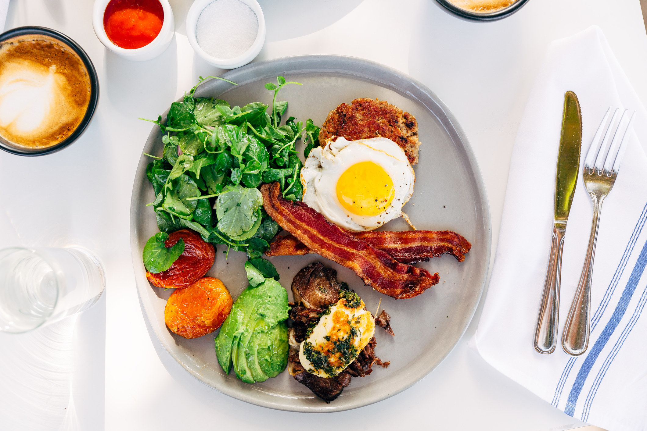 A plate of food including bacon, egg, and avocado.