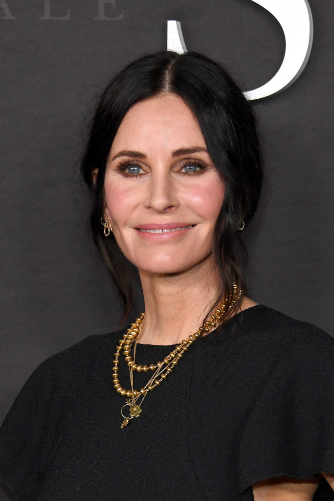 Close-up of Courteney smiling and wearing several necklaces
