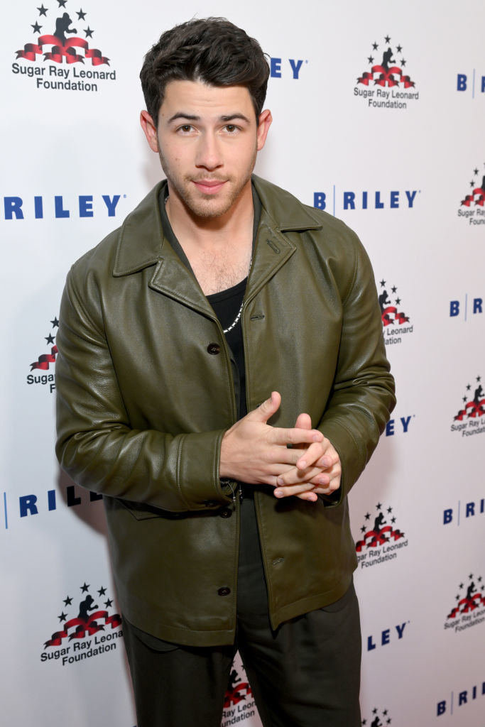Nick with his hand clasped in front of him, wearing a leather jacket