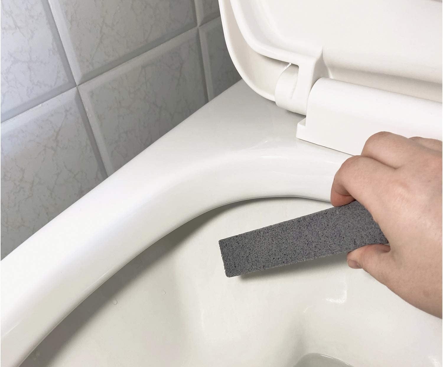 person using a pumice stick to clean a toilet