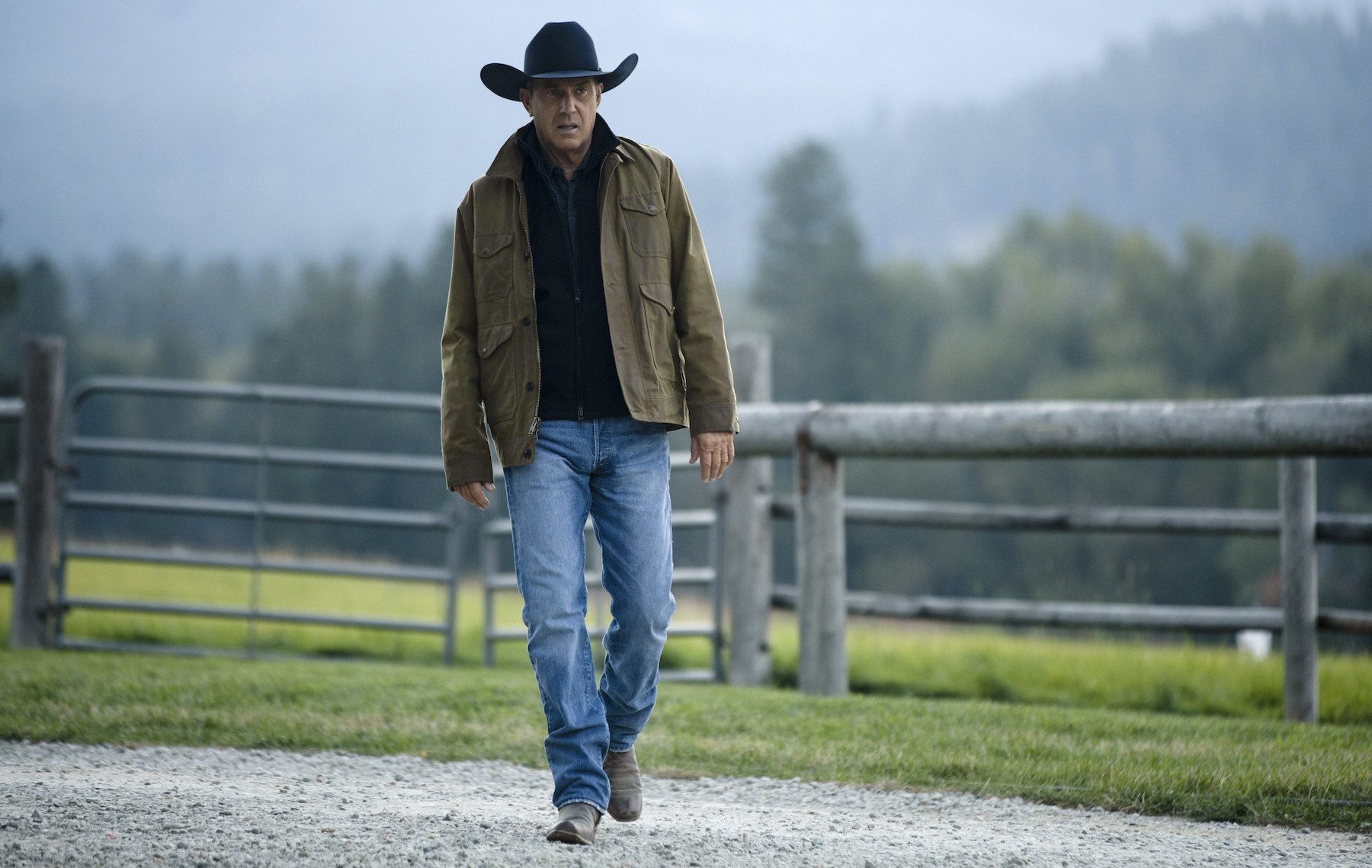 A man in cowboy attire walks around the grounds of his ranch alone