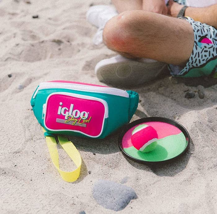 the insulated cooler fanny on a beach beside a ball and a frisbee