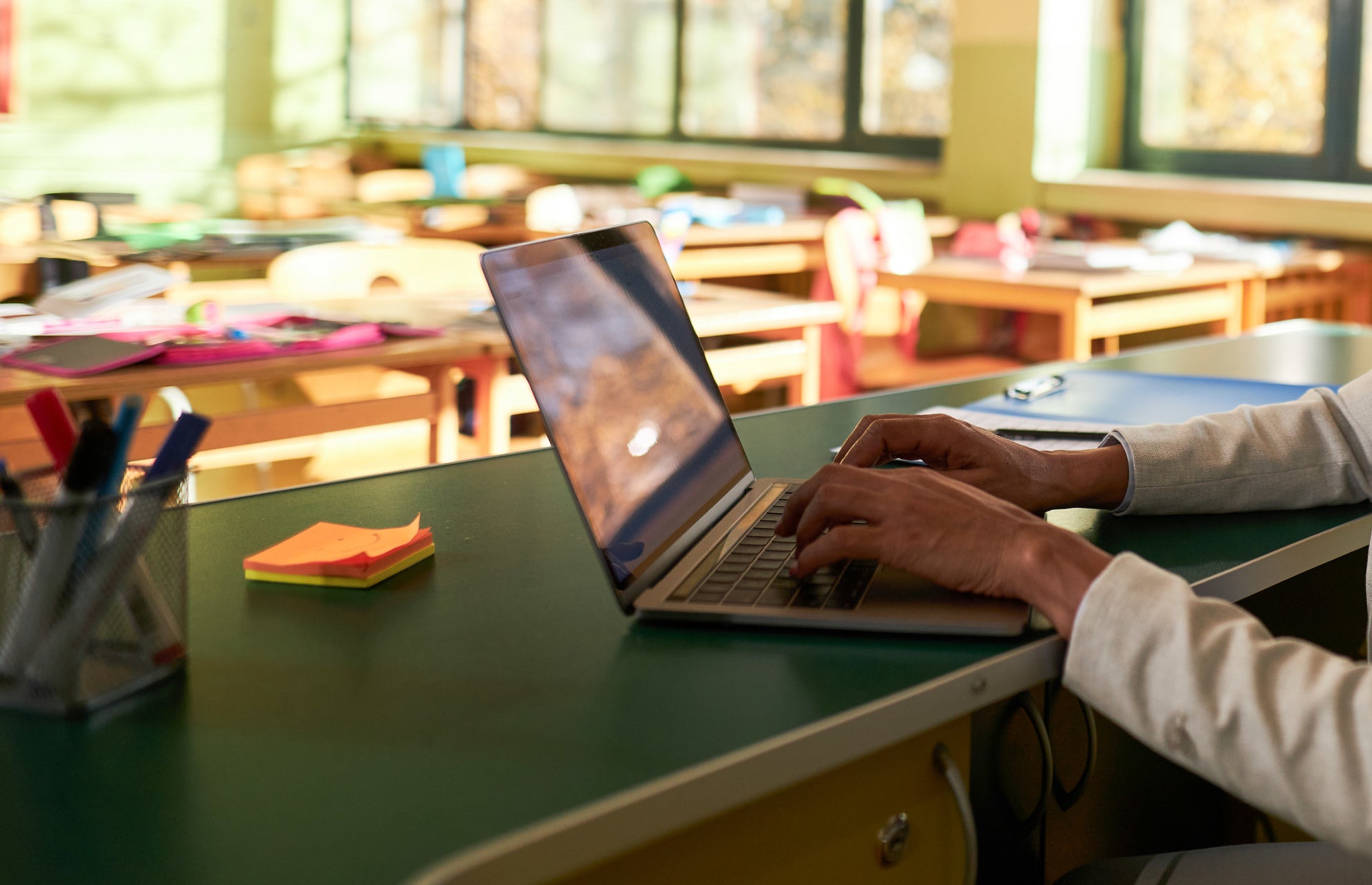 a teacher types on their laptop at their desk in their classroom