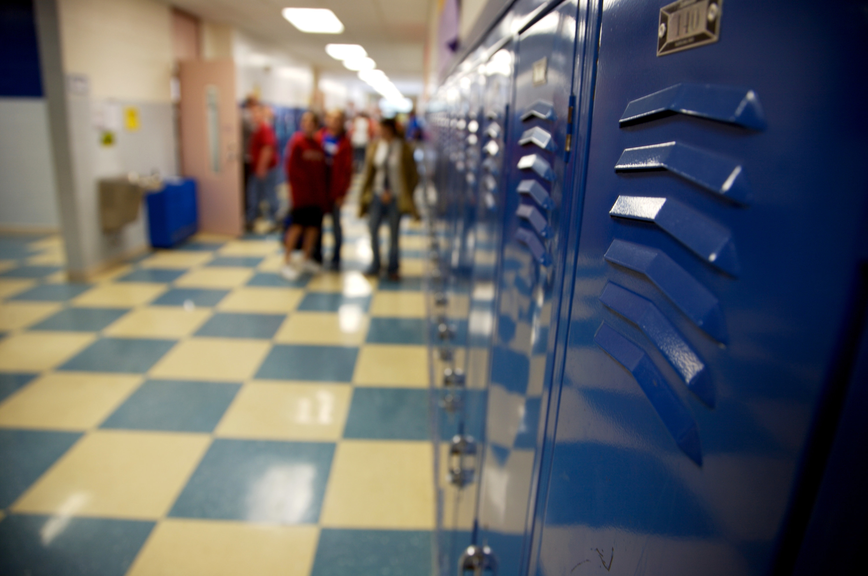 blurred students walking through a hall filled with lockers