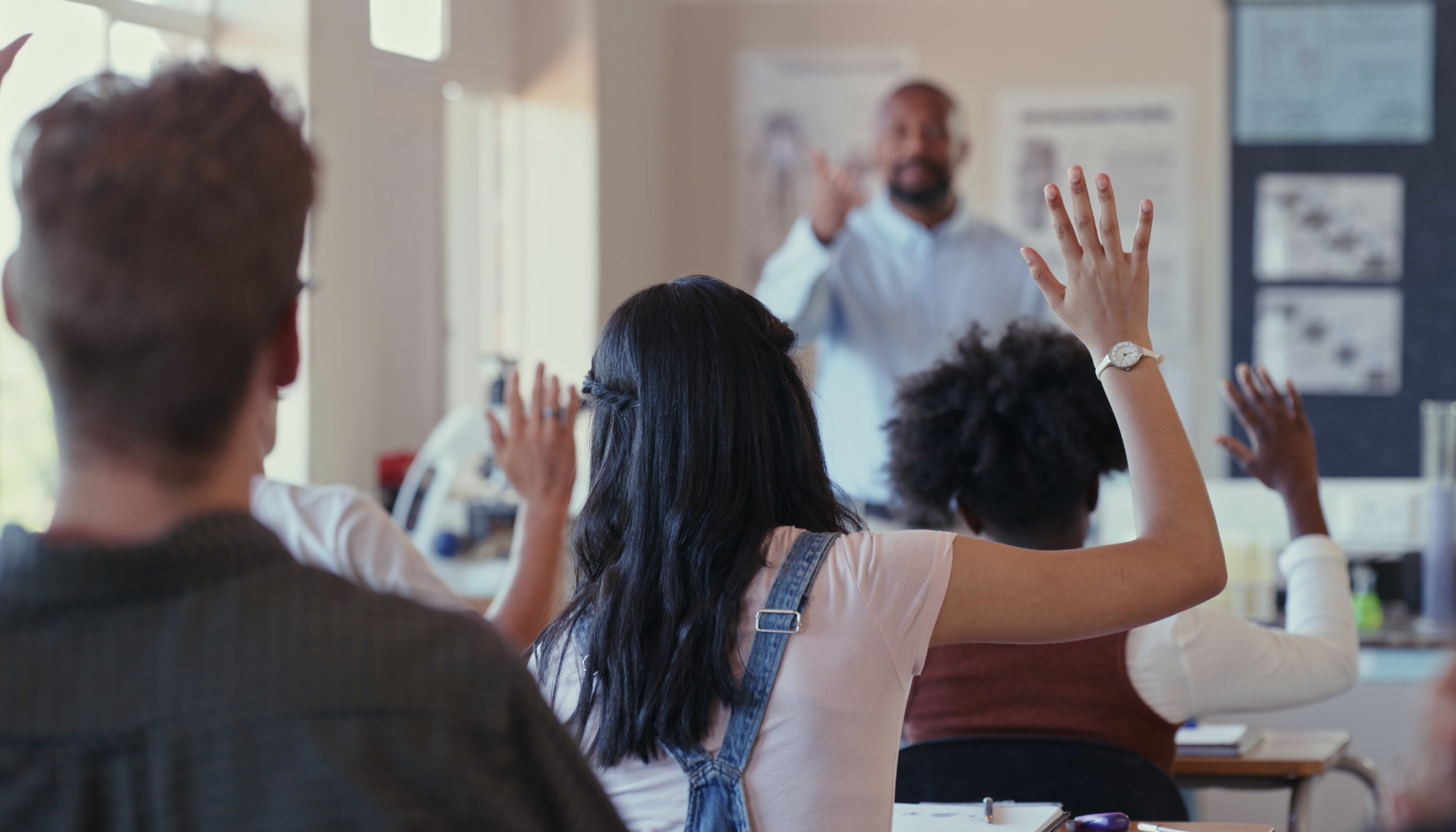 students raise hands as a teacher asks a question