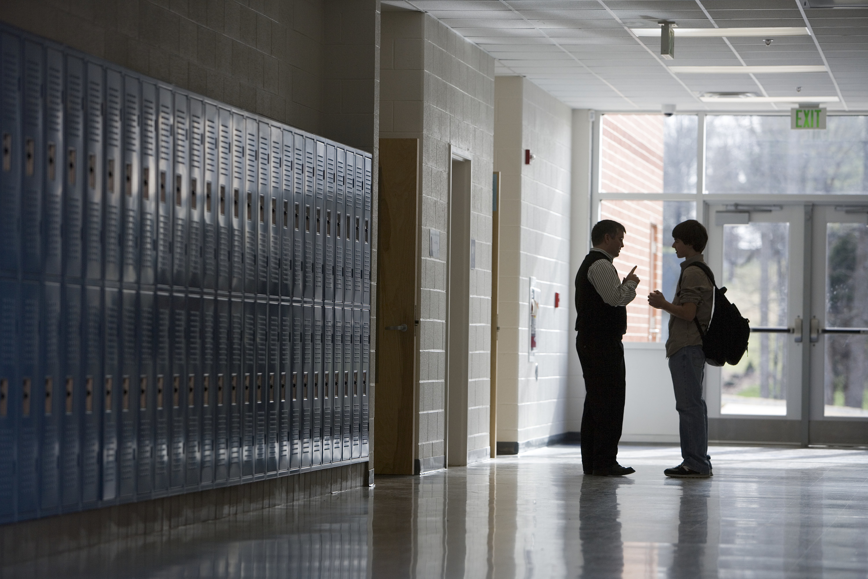 a teacher speaks to a student in an empty hallway