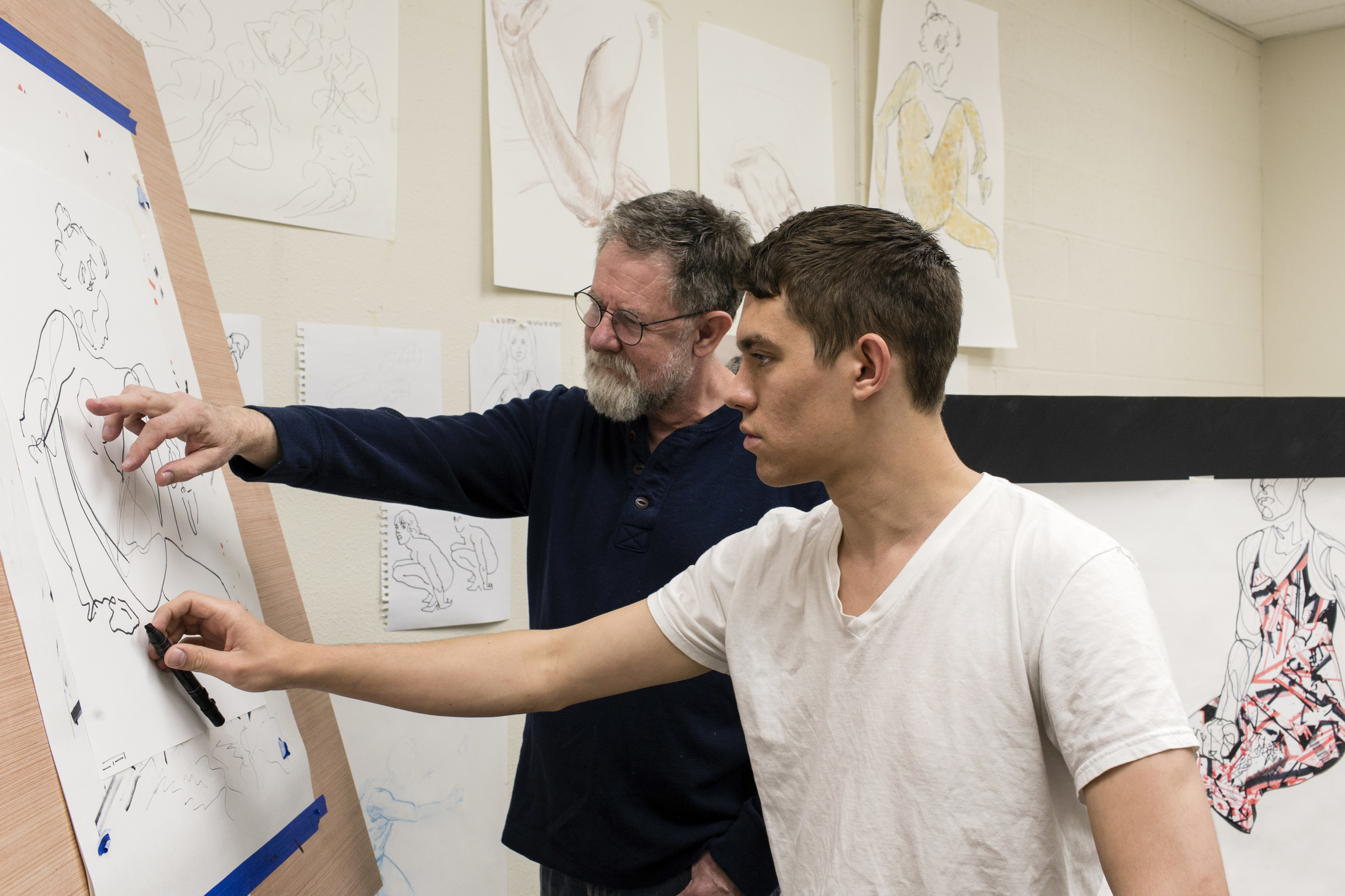 A man offers guidance to a young artist working on a drawing