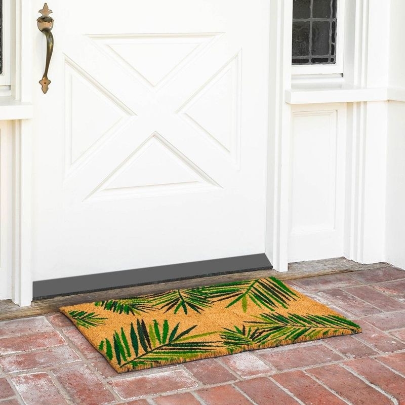a green palm doormat laying on the front porch