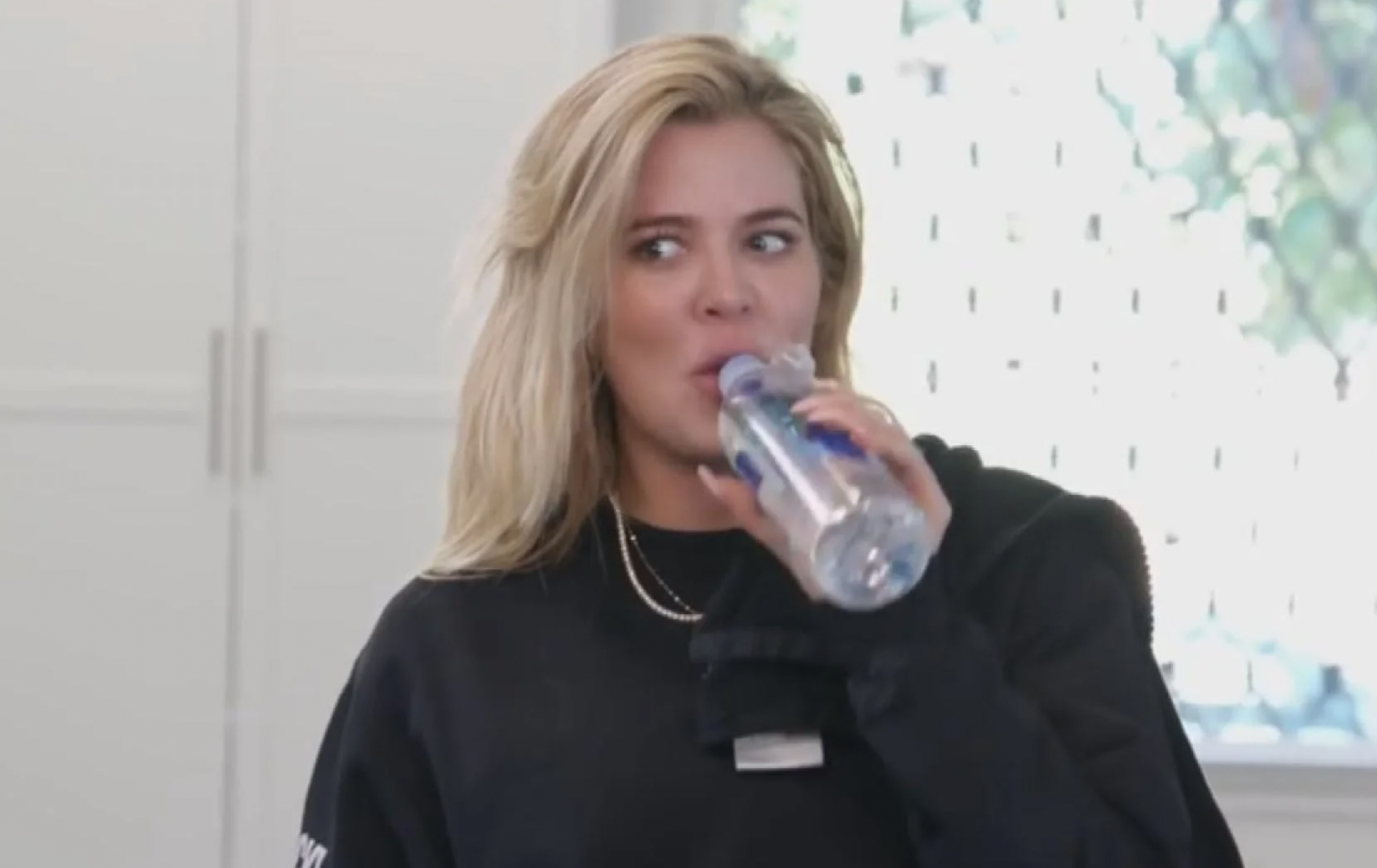 A screenshot of Khloe Kardashian sipping from a water bottle and giving someone an incredulous side-eye