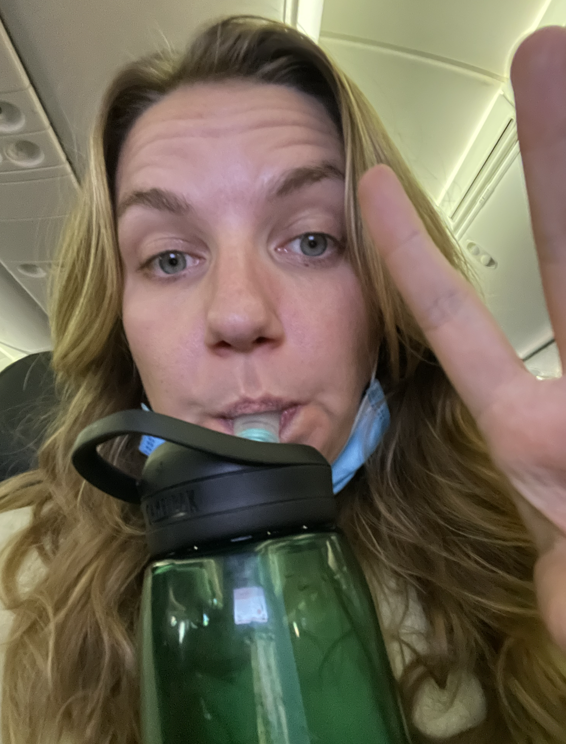 A selfie of a girl sitting in a plane seat, she&#x27;s sipping from a water bottle
