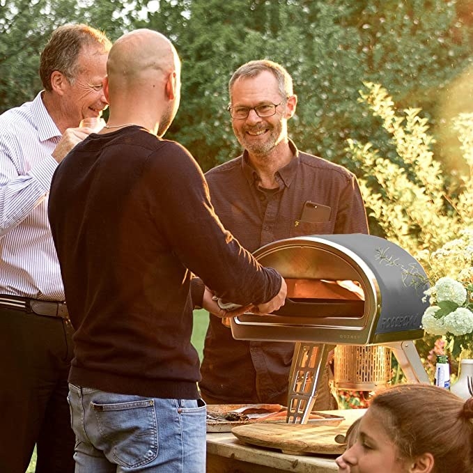 A small group of people crowded around the pizza oven at a party