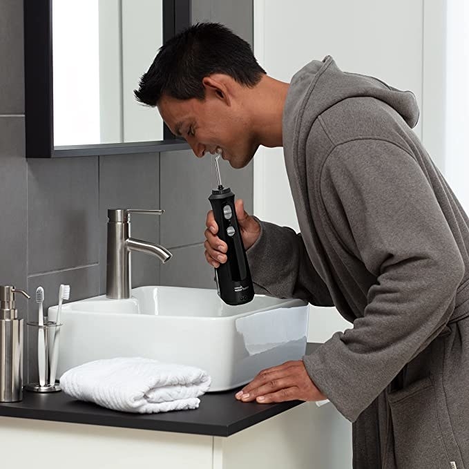 Model flossing teeth over bathroom sink with the portable waterpik