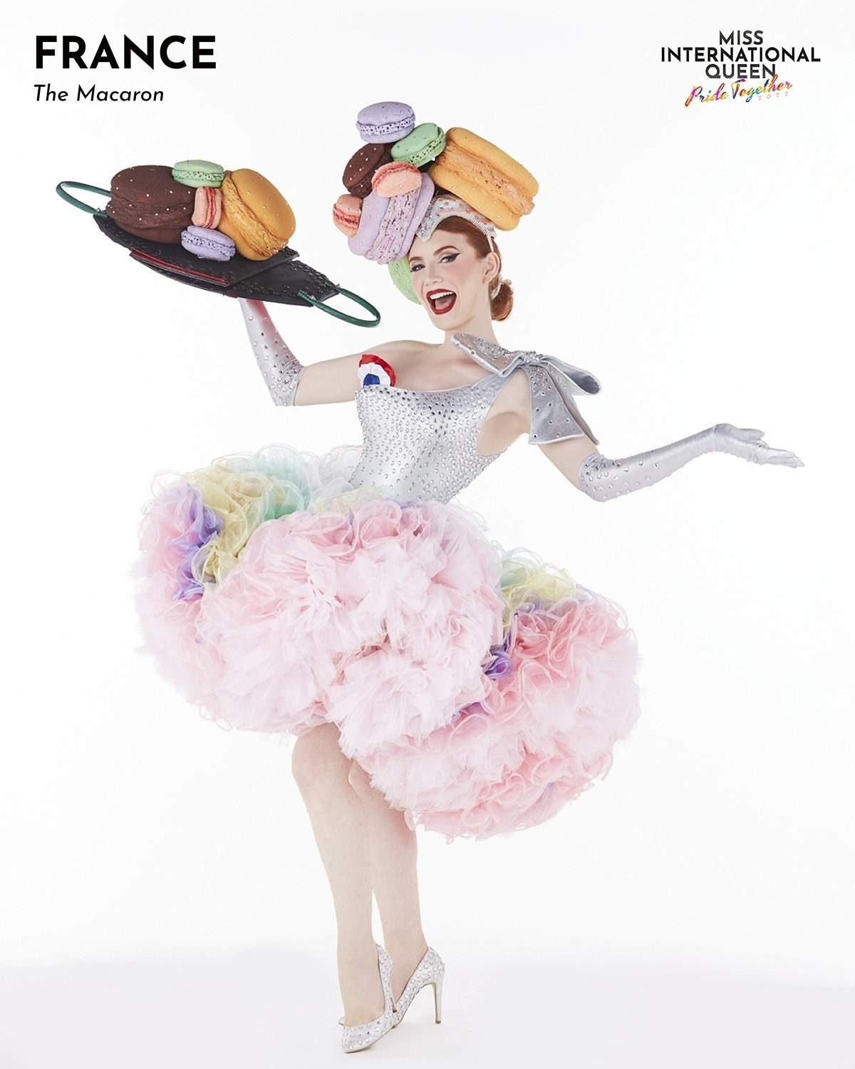Miss France in an outfit with a macaron hat and holds a macaron tray