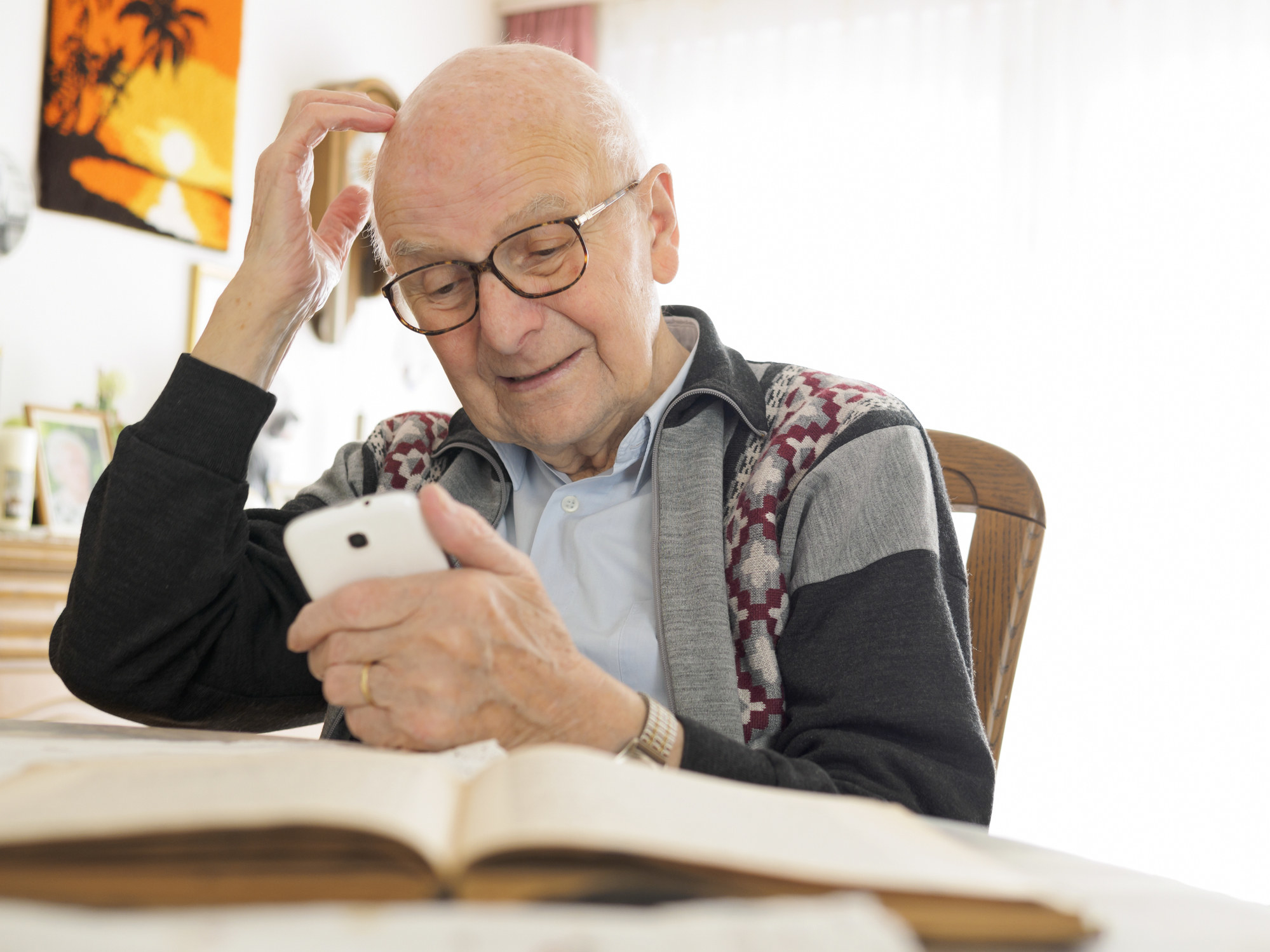 an older person at a table with a book open and phone in their hand