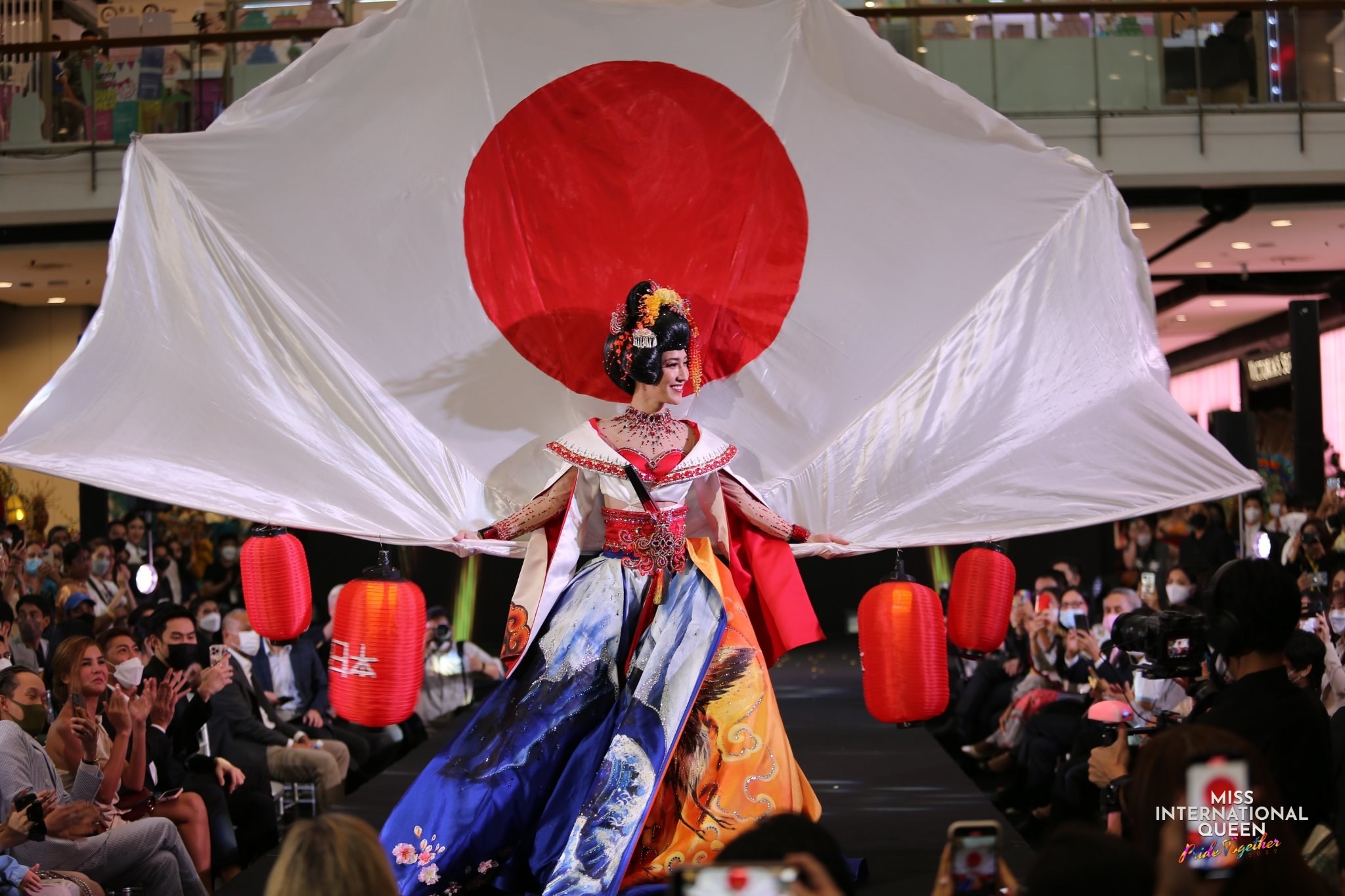 Miss Japan walks the runway with a Japanese flag fan and lanterns