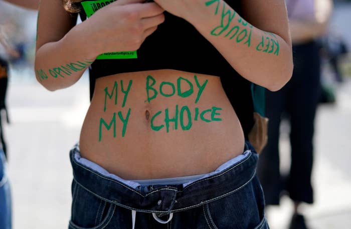 The words &quot;My body. My choice&quot; are written in green paint on a person&#x27;s stomach
