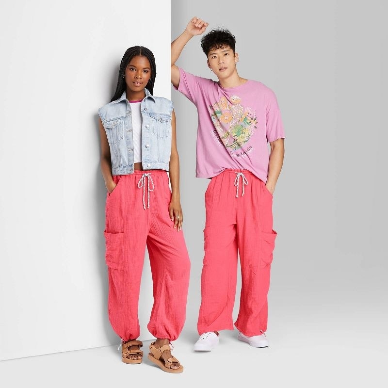 model wearing pink pants, tan shoes, a white top and blue vest and 2nd model wearing pink pants, white sneakers and pink colorful  top