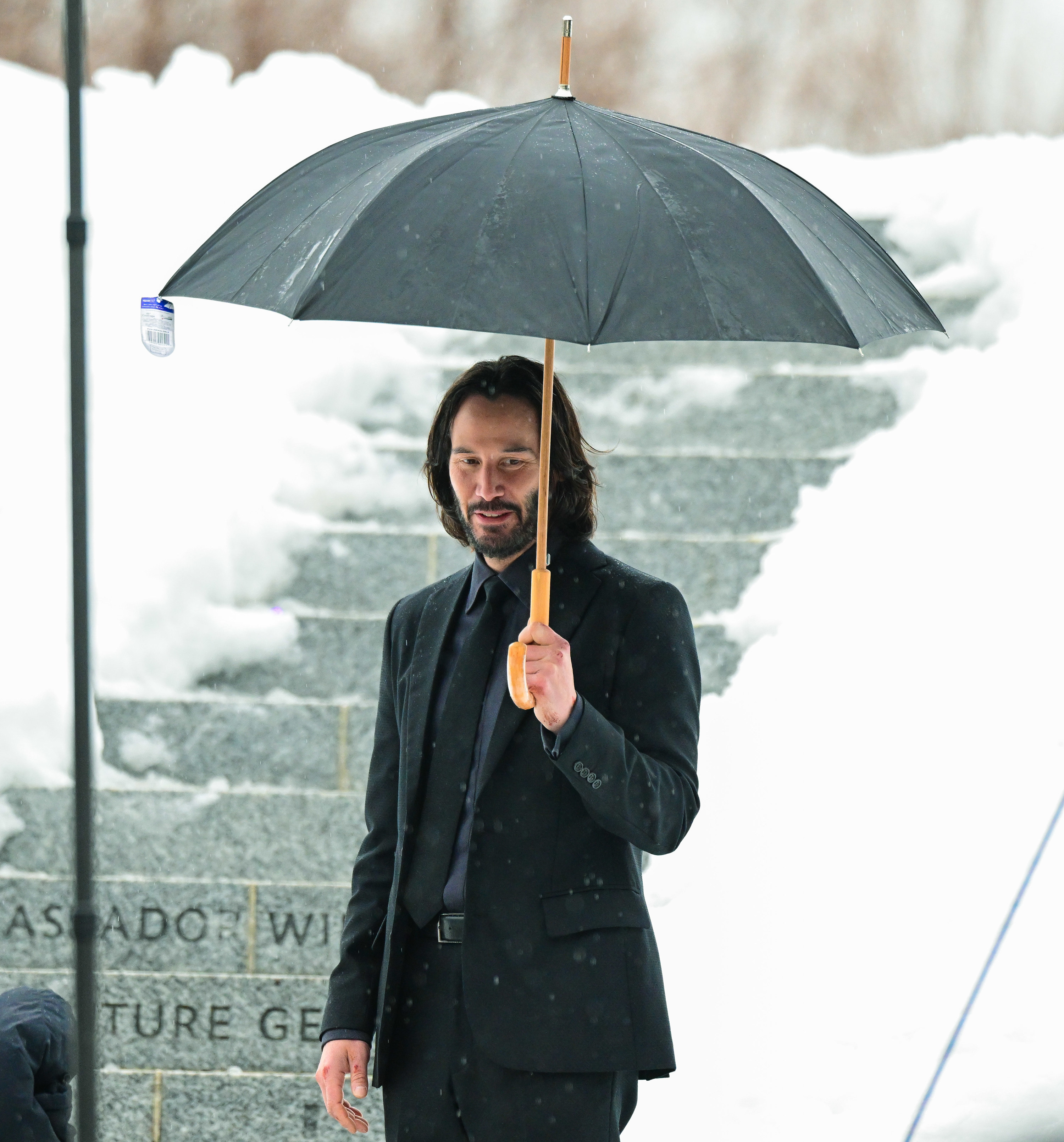 Keanu smiling while holding an umbrella in the snow