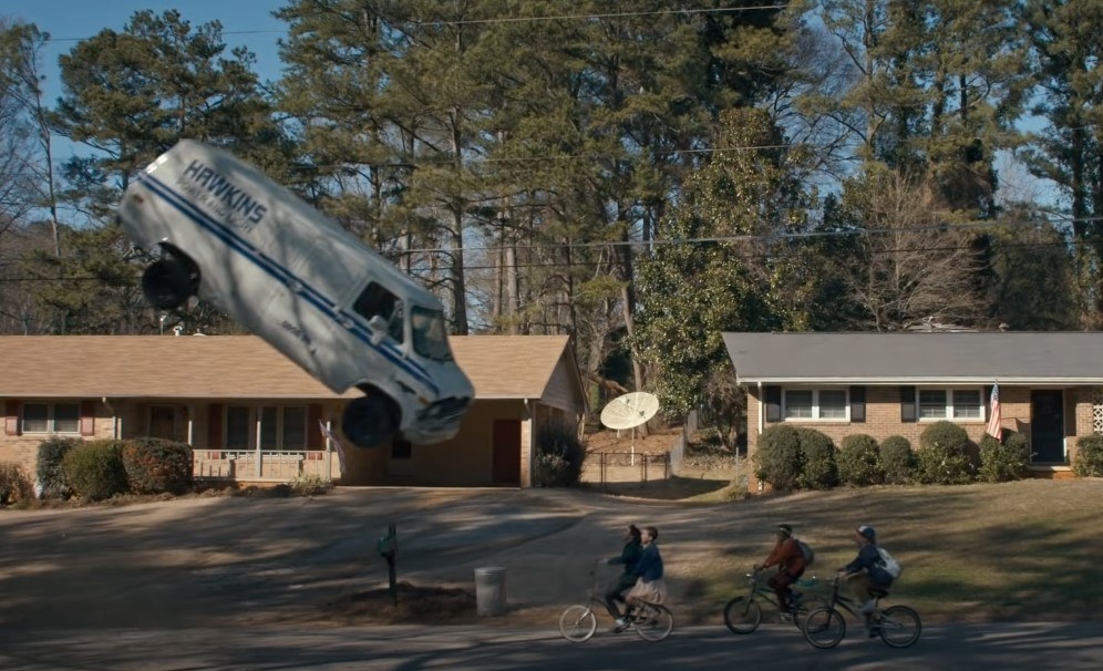 Image shows a van flying through the air over four kids on bicycles