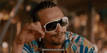 A man wearing sunglasses and with grill on his teeth is holding a cigarette while screaming &quot;Spring Break&quot;