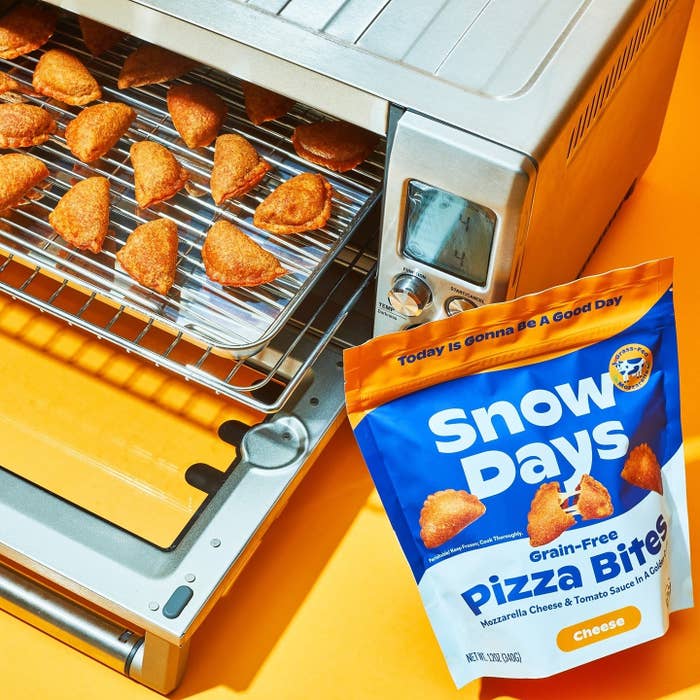 The pizza bites on a tray in a toaster oven next to the bag
