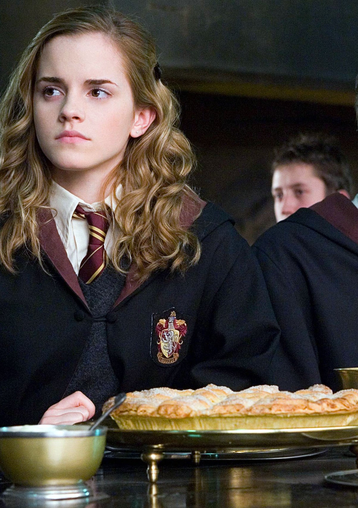 Emma Watson as Hermione Granger sits at a table in the Great Hall of Hogwarts