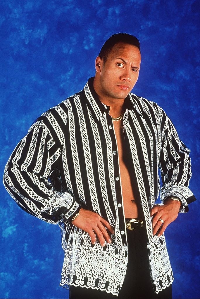 the rock posing with his hands on his hips wearing a vest