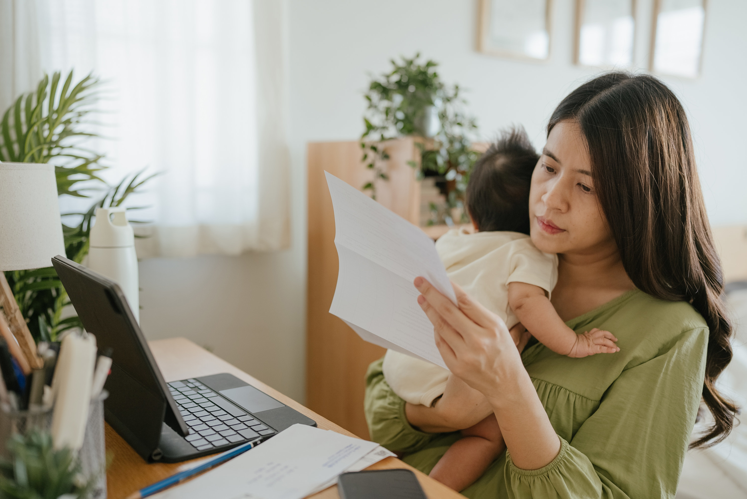 stressed out mom holding a baby while looking at bills