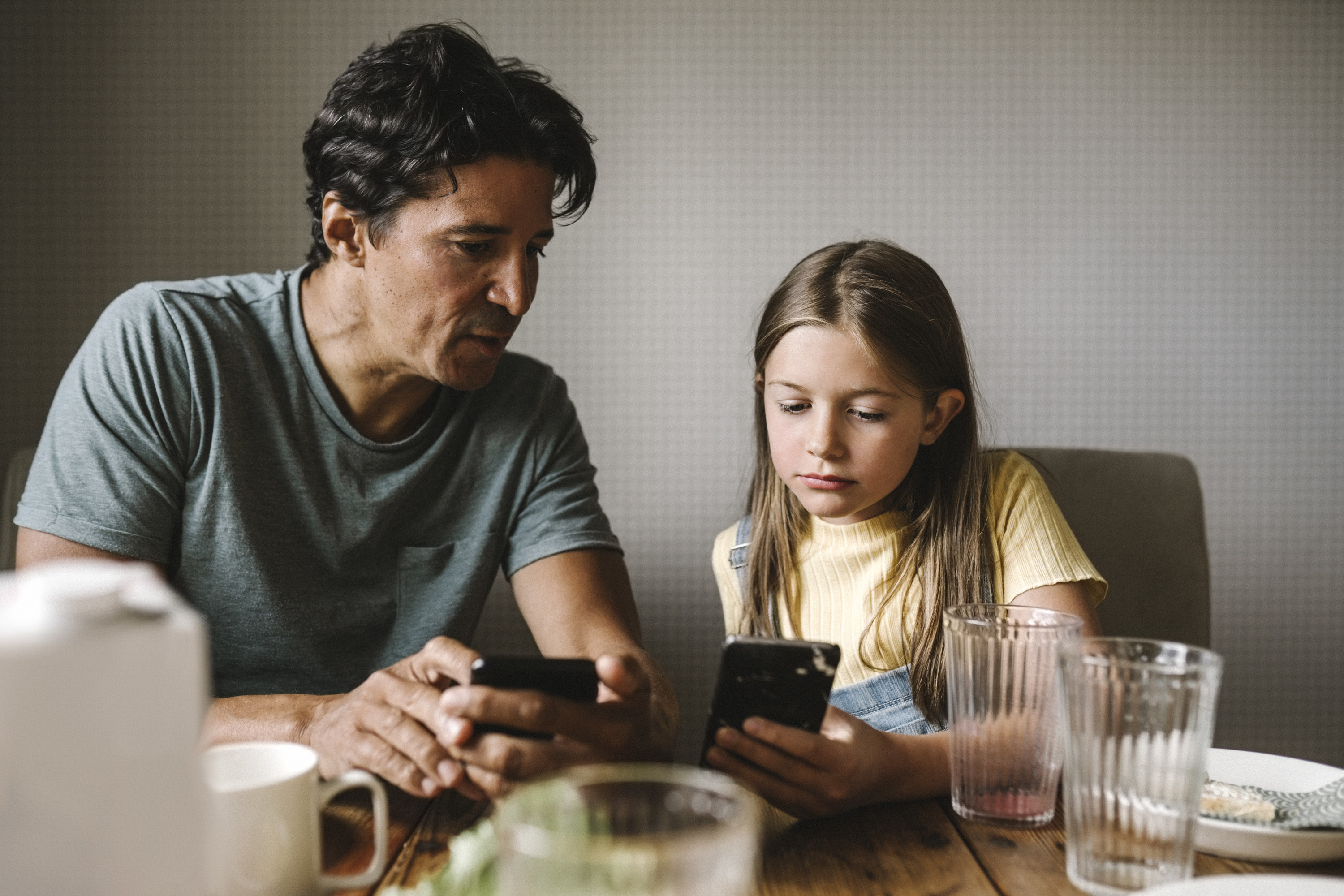 a dad and daughter looking at their phones