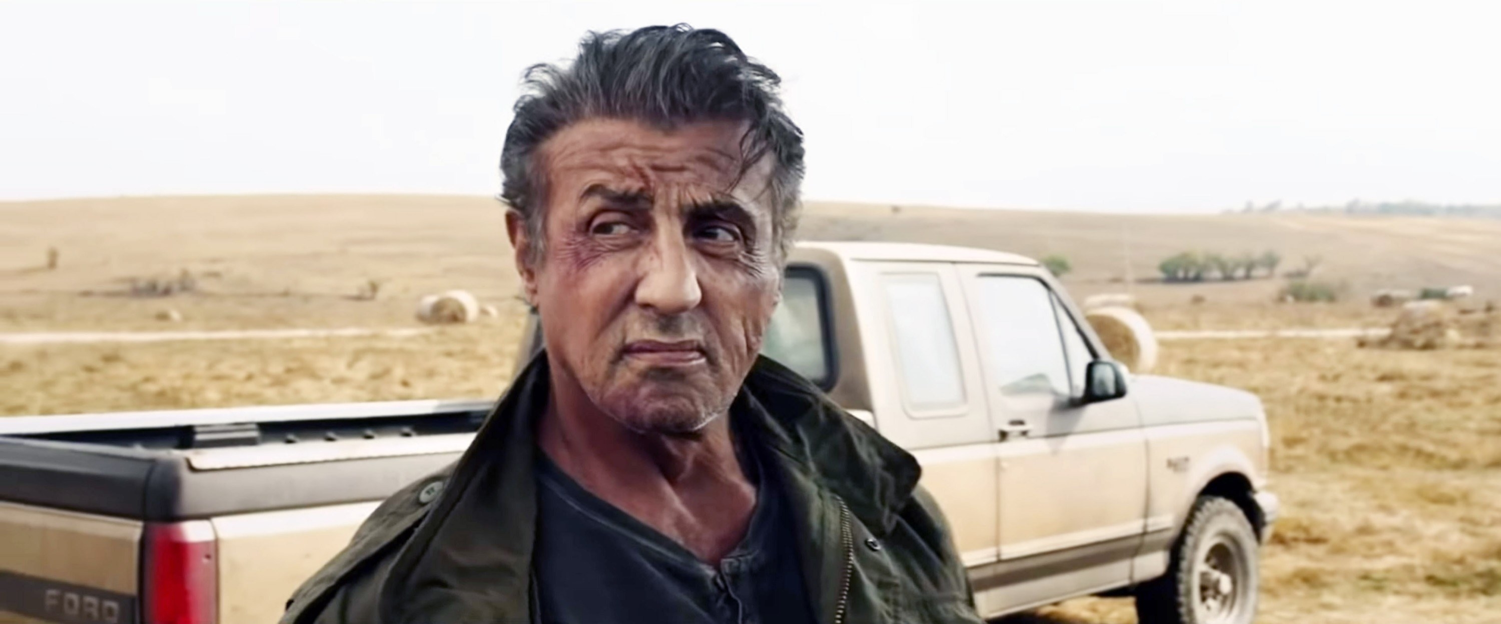 An older Sylvester as Rambo standing in front of a pickup truck